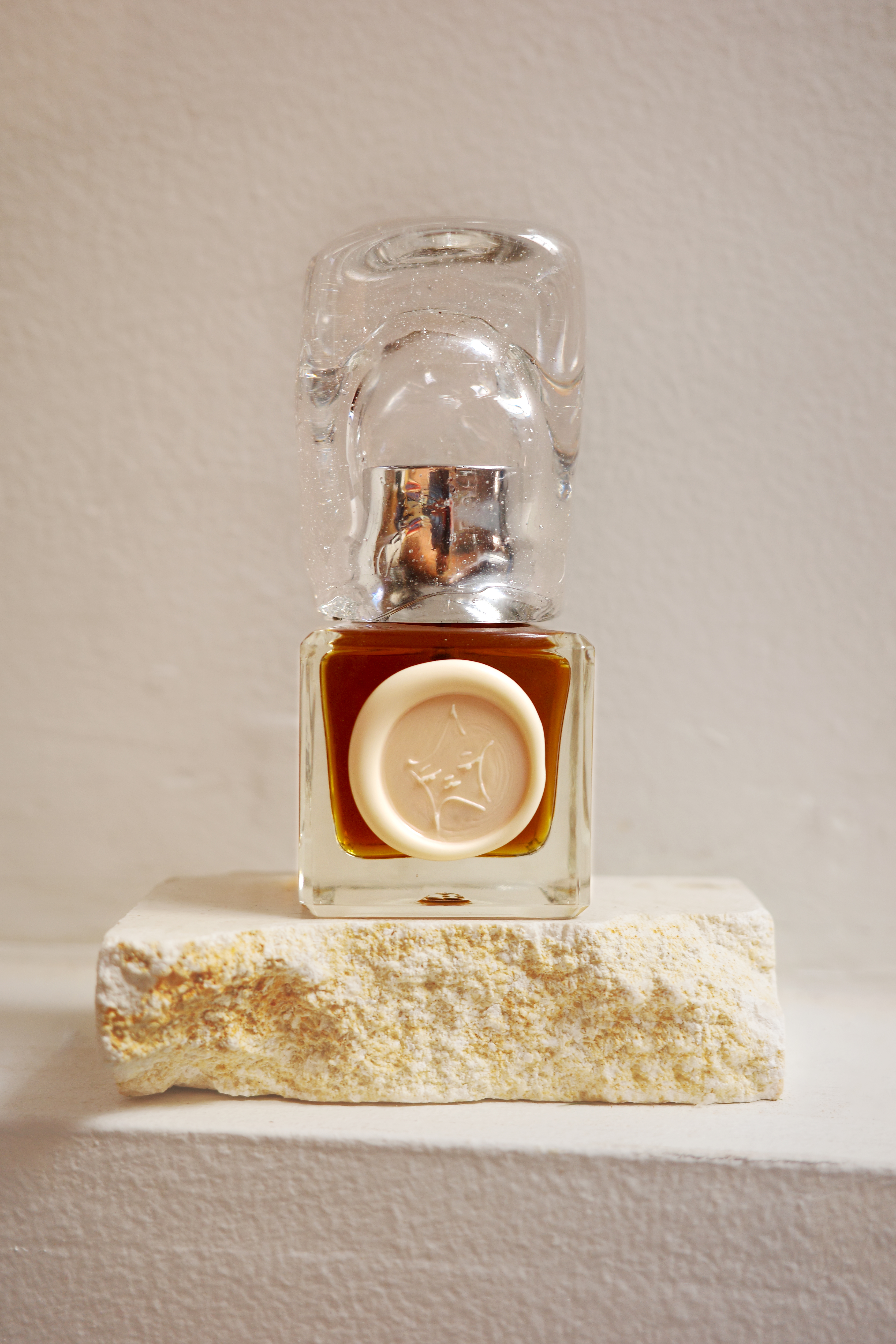 a product photo of the full sized perfume, with a handmade glass top, wax seal of the star girl in pearlescent white, and rich amber liquid
